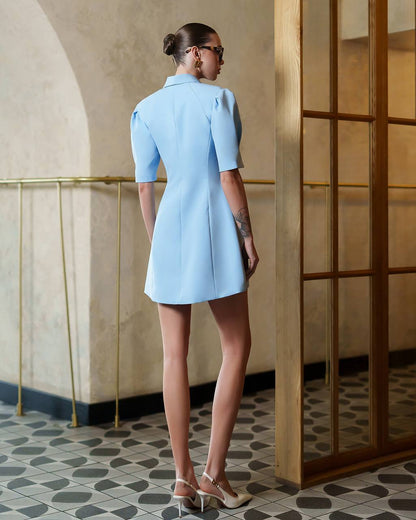Woman wearing a light blue dress standing in a room with a decorative wall and floor.