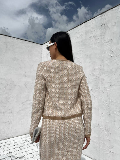 Woman in a beige tweed suit standing against a white wall with blue sky.
