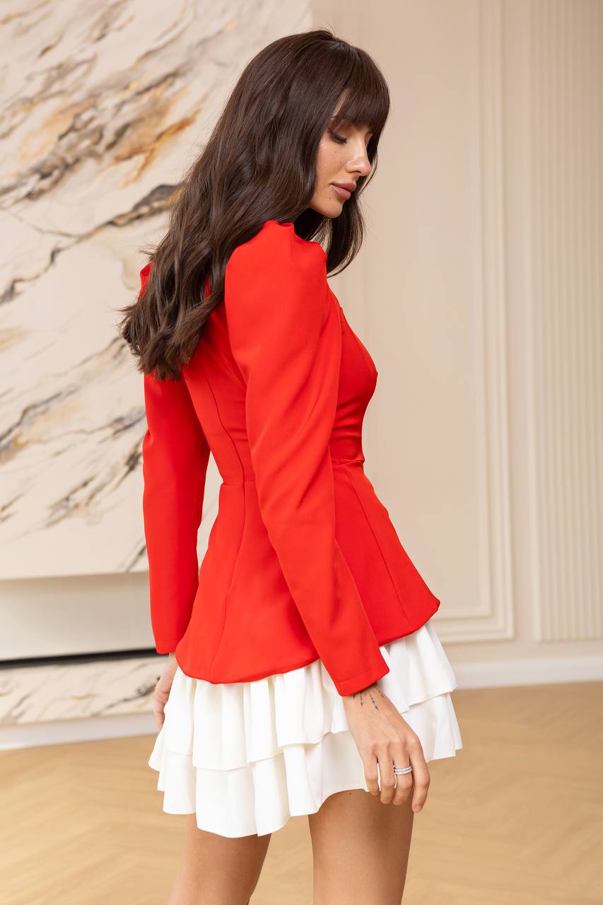 Woman wearing a red blazer over a white dress with a marble wall background