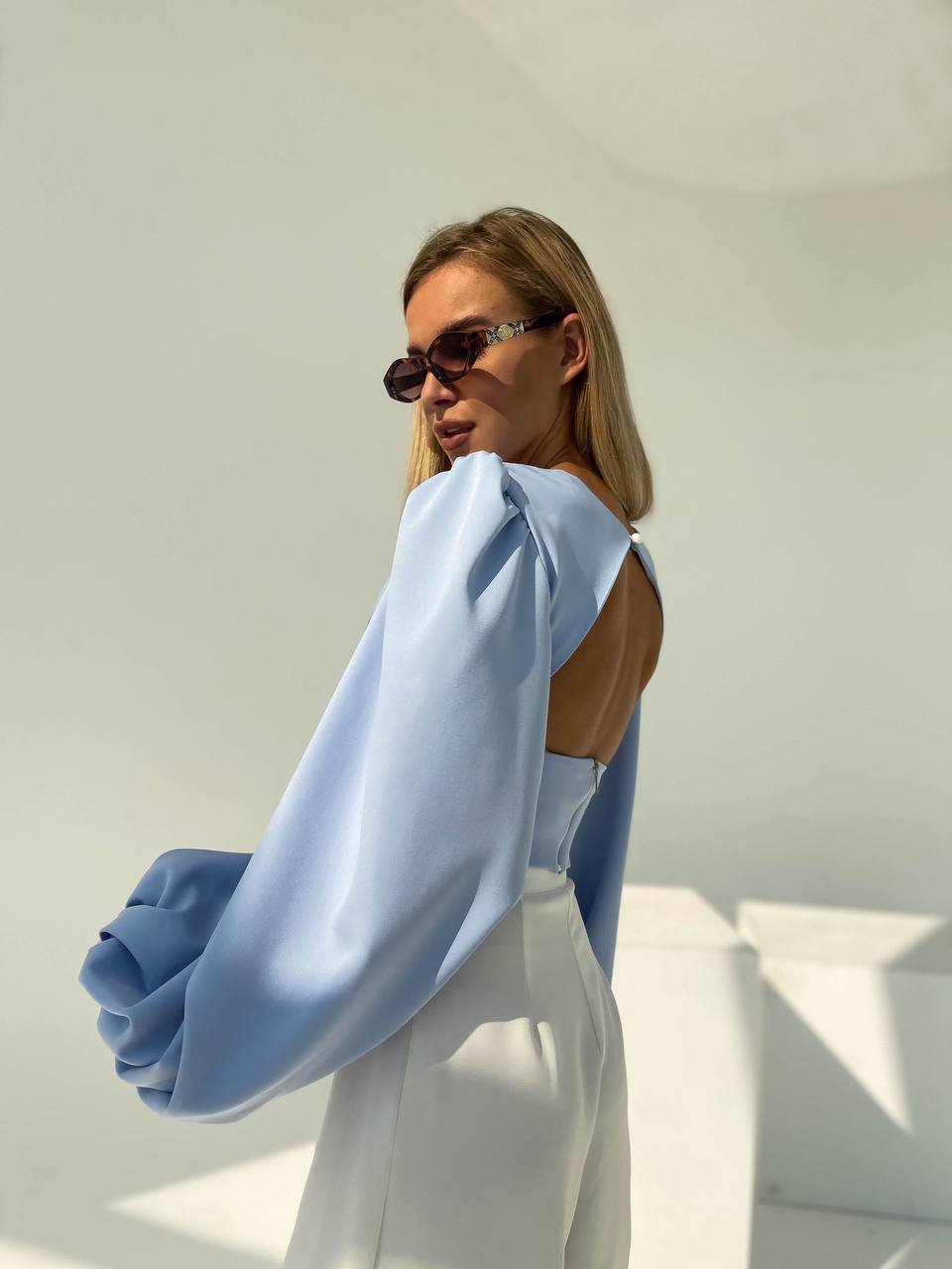Person wearing a light blue blouse with a cut-out design and white pants against a white background