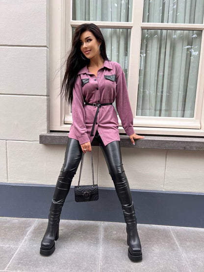 Woman in pink shirt and black leather pants standing on a sidewalk.