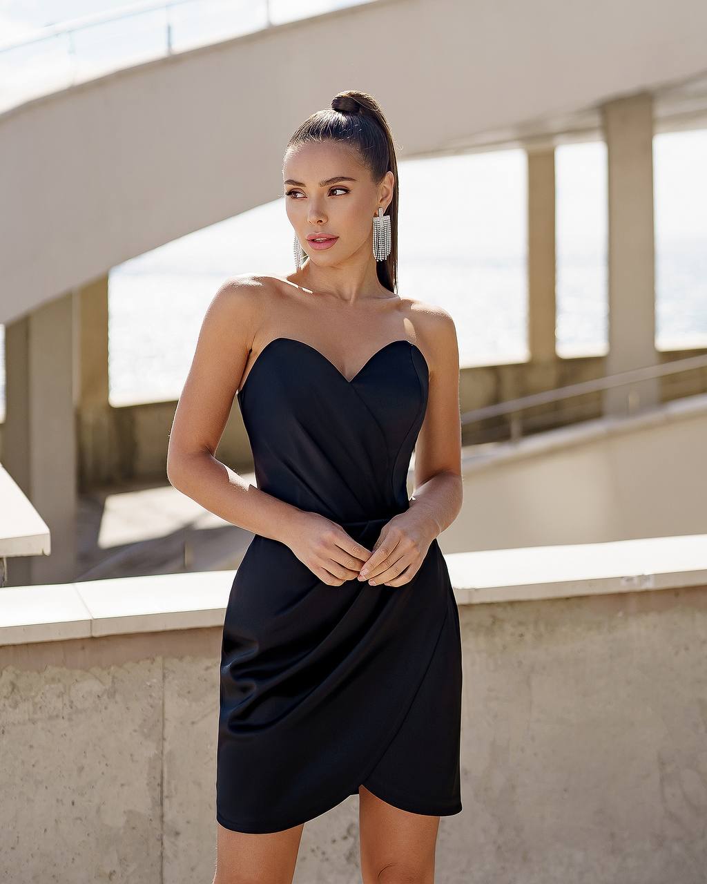 Woman wearing a black strapless dress standing outdoors.