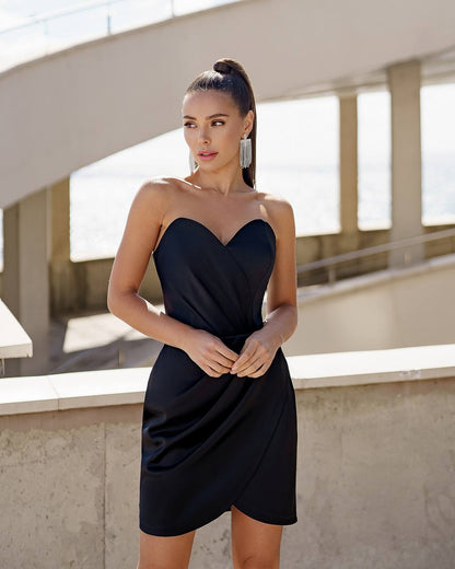 Woman wearing a black strapless dress standing outdoors.