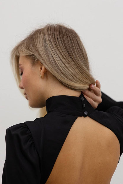 Person wearing a black open-back top against a white background