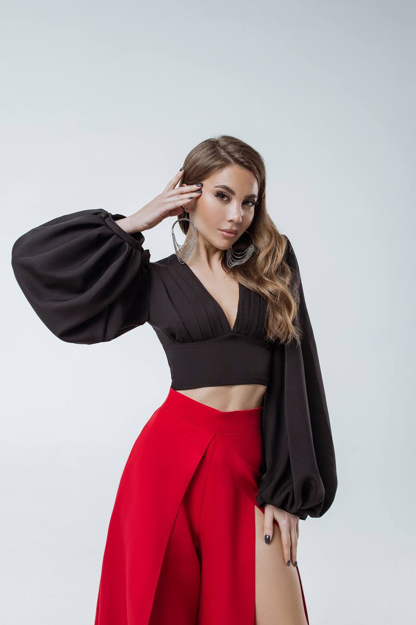 Woman wearing a black top with balloon sleeves and red pants on a white background