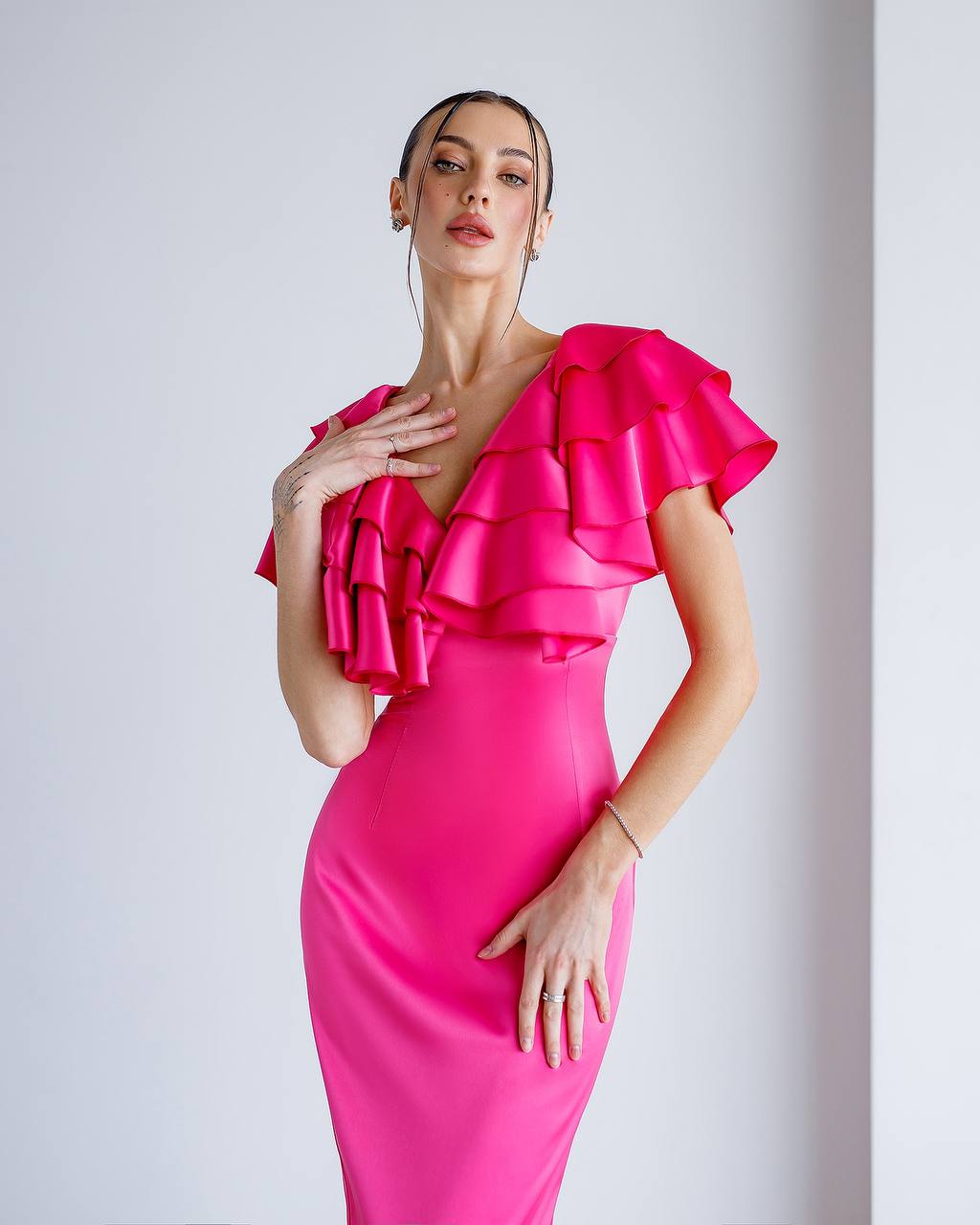 Woman wearing a bright pink dress with ruffled shoulders against a light gray background