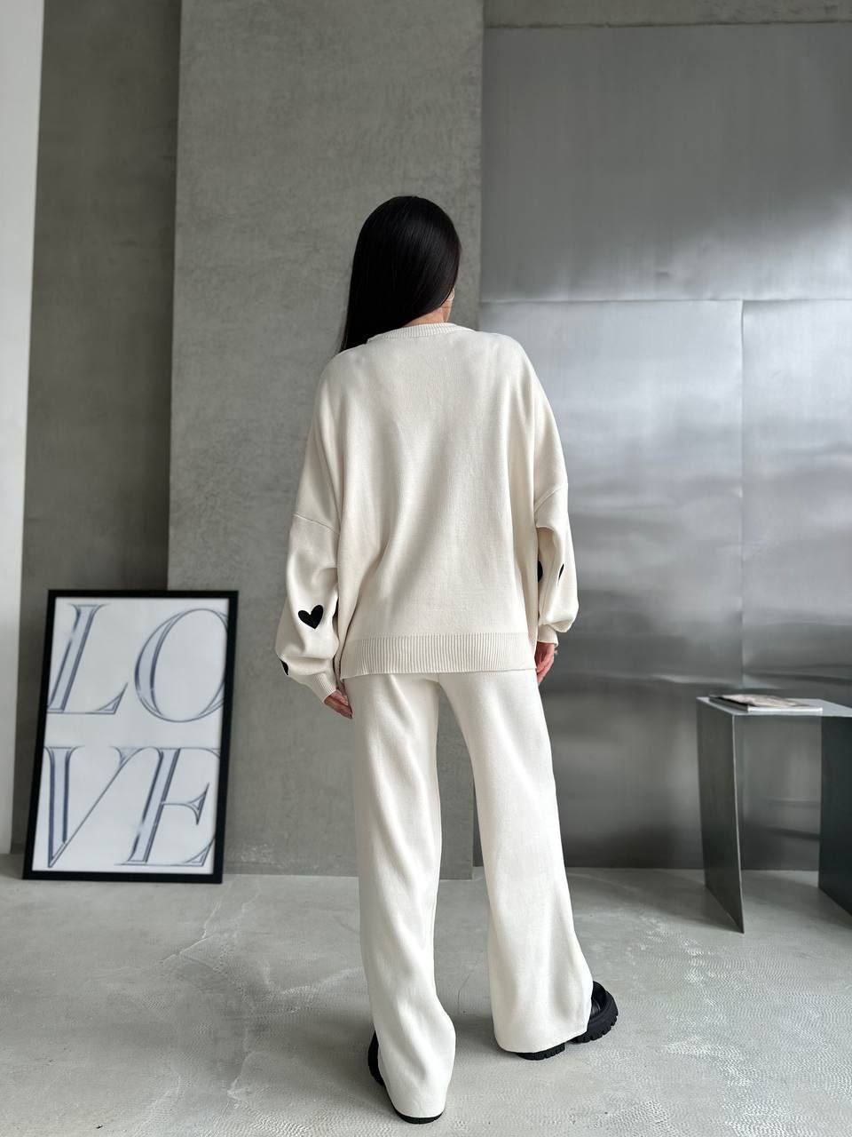 Person wearing a white outfit standing in a minimalistic room with a 'LOVE' sign on the wall.