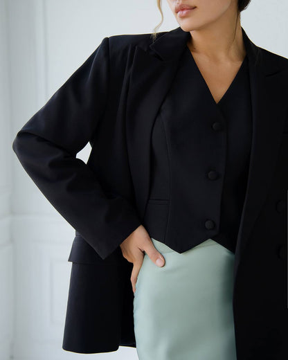 Person wearing a black blazer and light green pants against a neutral background
