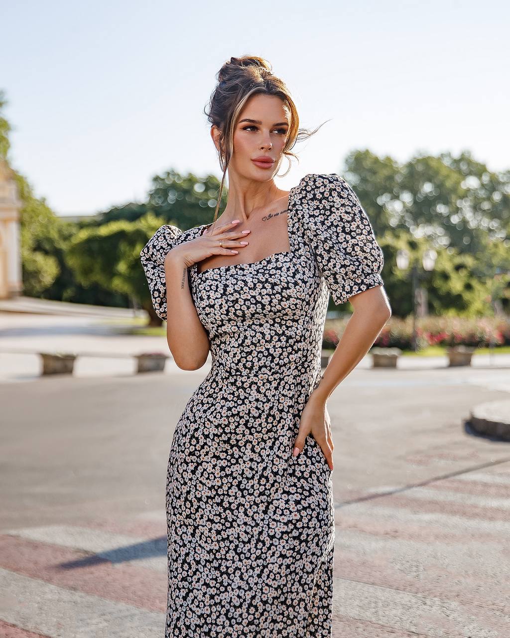 Woman in a floral dress standing outdoors with trees and a building in the background