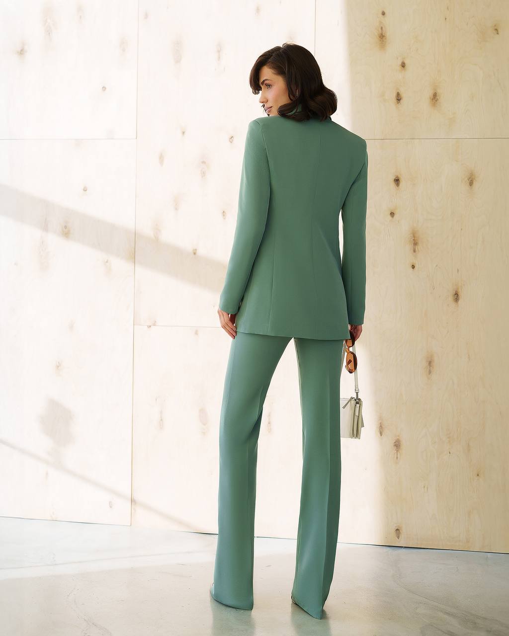 Woman wearing a green suit standing in a bright room with wooden walls.