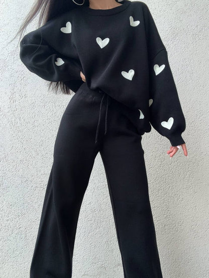 Person wearing a black sweater with white heart patterns against a light gray background
