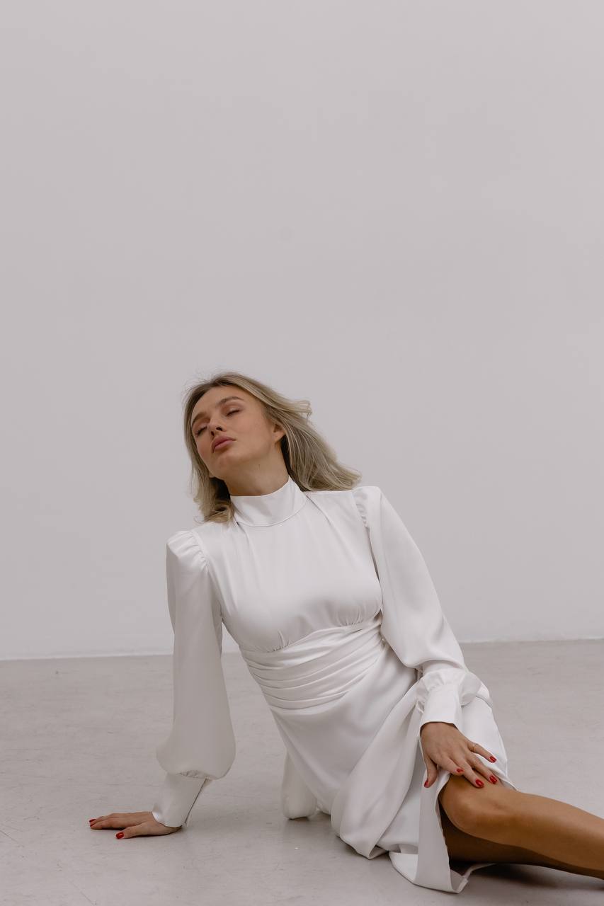 Woman in a white dress sitting on the floor against a plain background