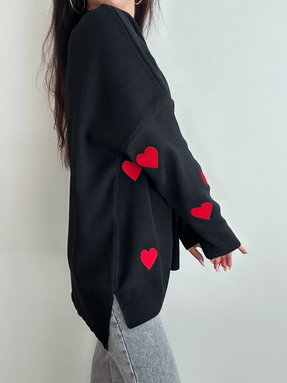 Black sweater with red heart patterns worn by a person on a plain background
