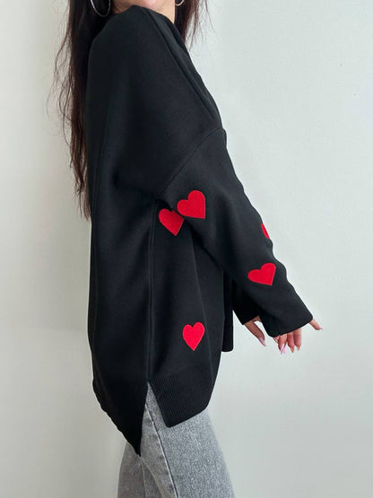 Black sweater with red heart patterns worn by a person on a plain background