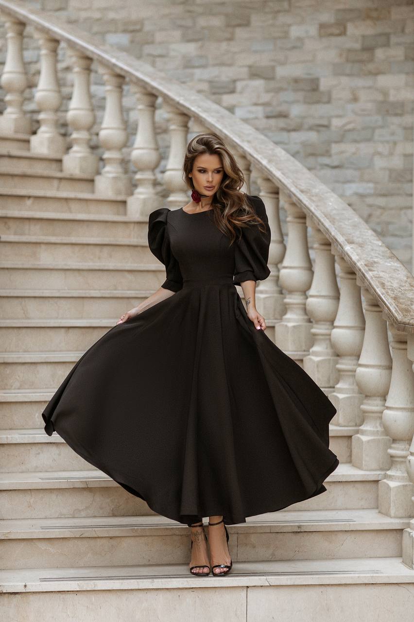 Woman in a black dress standing on a staircase with a stone wall background