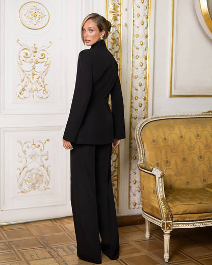 Woman in a black suit standing in an ornate room with gold accents.