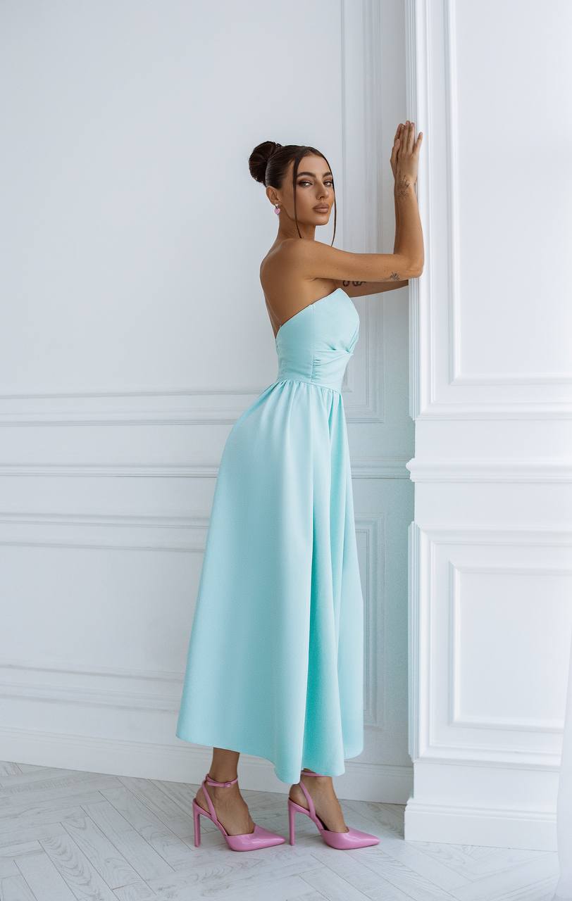 Woman in a light blue strapless dress standing against a white wall.