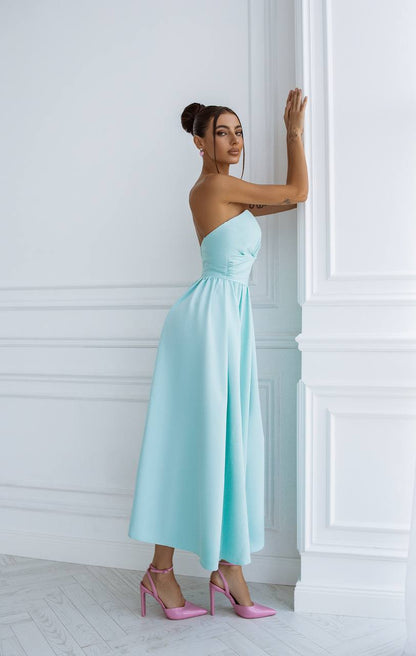 Woman in a light blue strapless dress standing against a white wall.