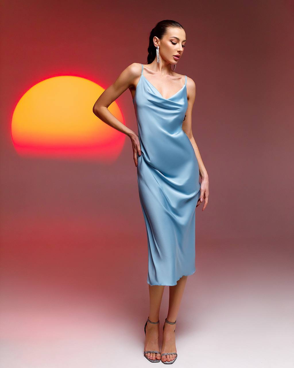 Woman in a light blue dress standing against a gradient background with a sun-like shape.