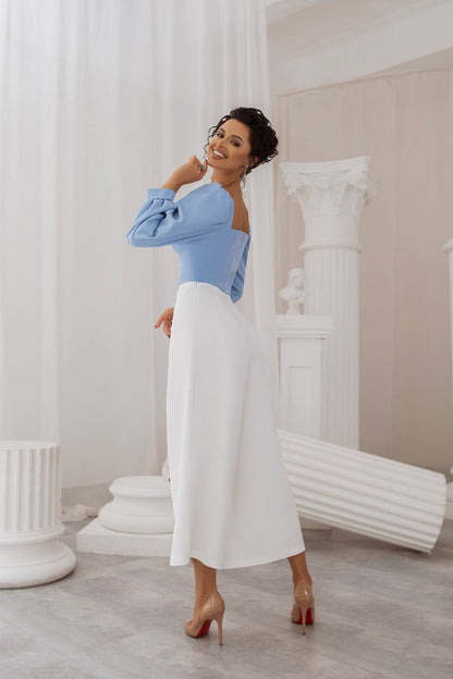 Woman in a blue top and white skirt standing in a classical setting with columns.