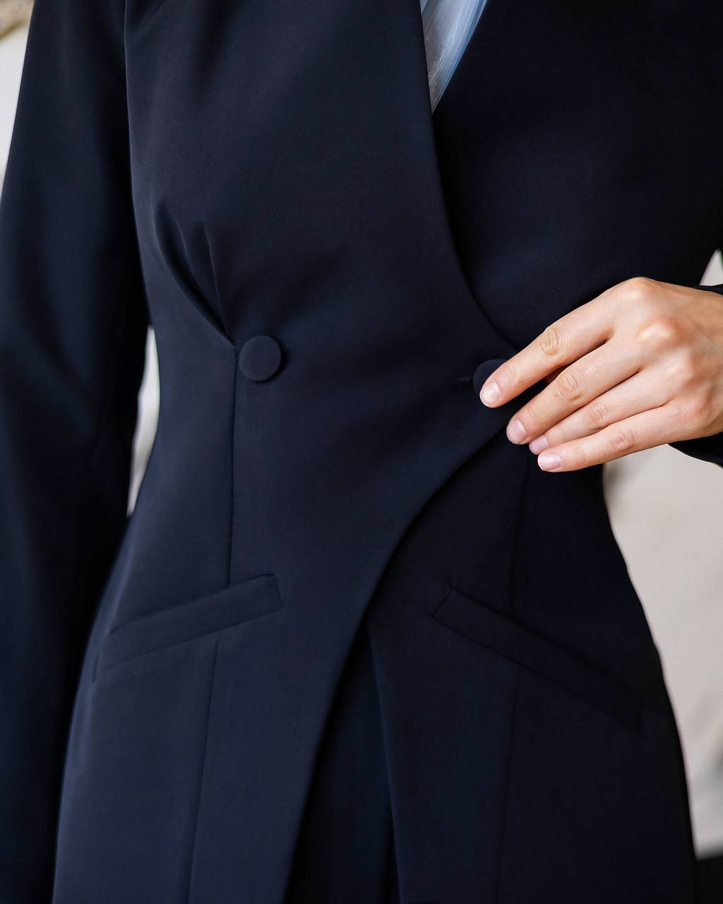 Navy blue suit jacket with a hand adjusting the button