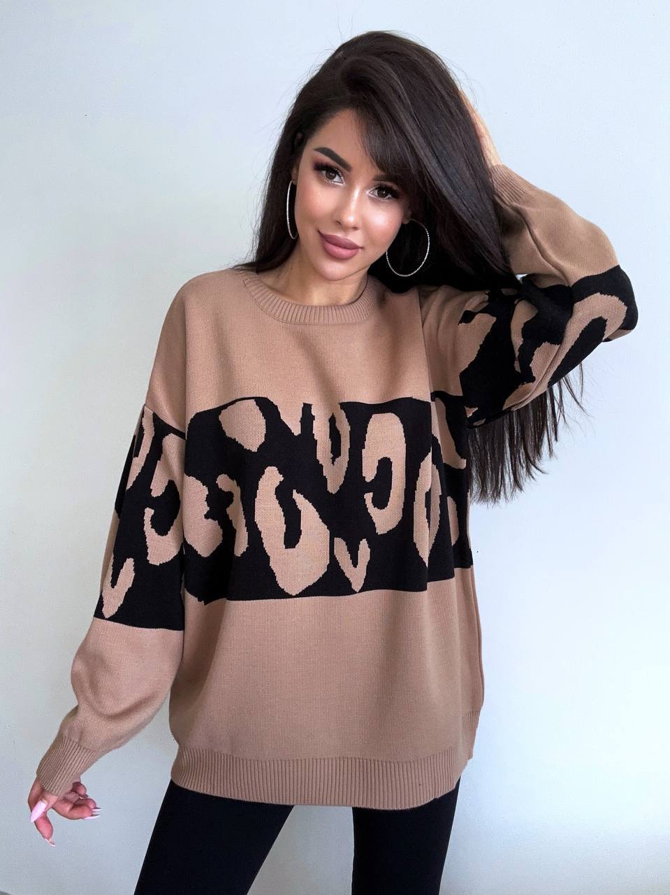 Woman wearing a beige sweater with black leopard print pattern against a white background