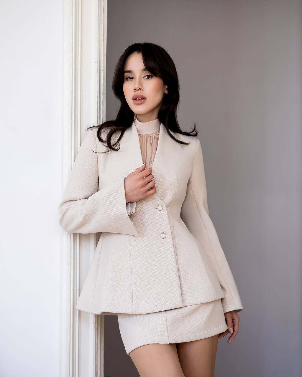 Woman wearing a beige suit standing against a plain background