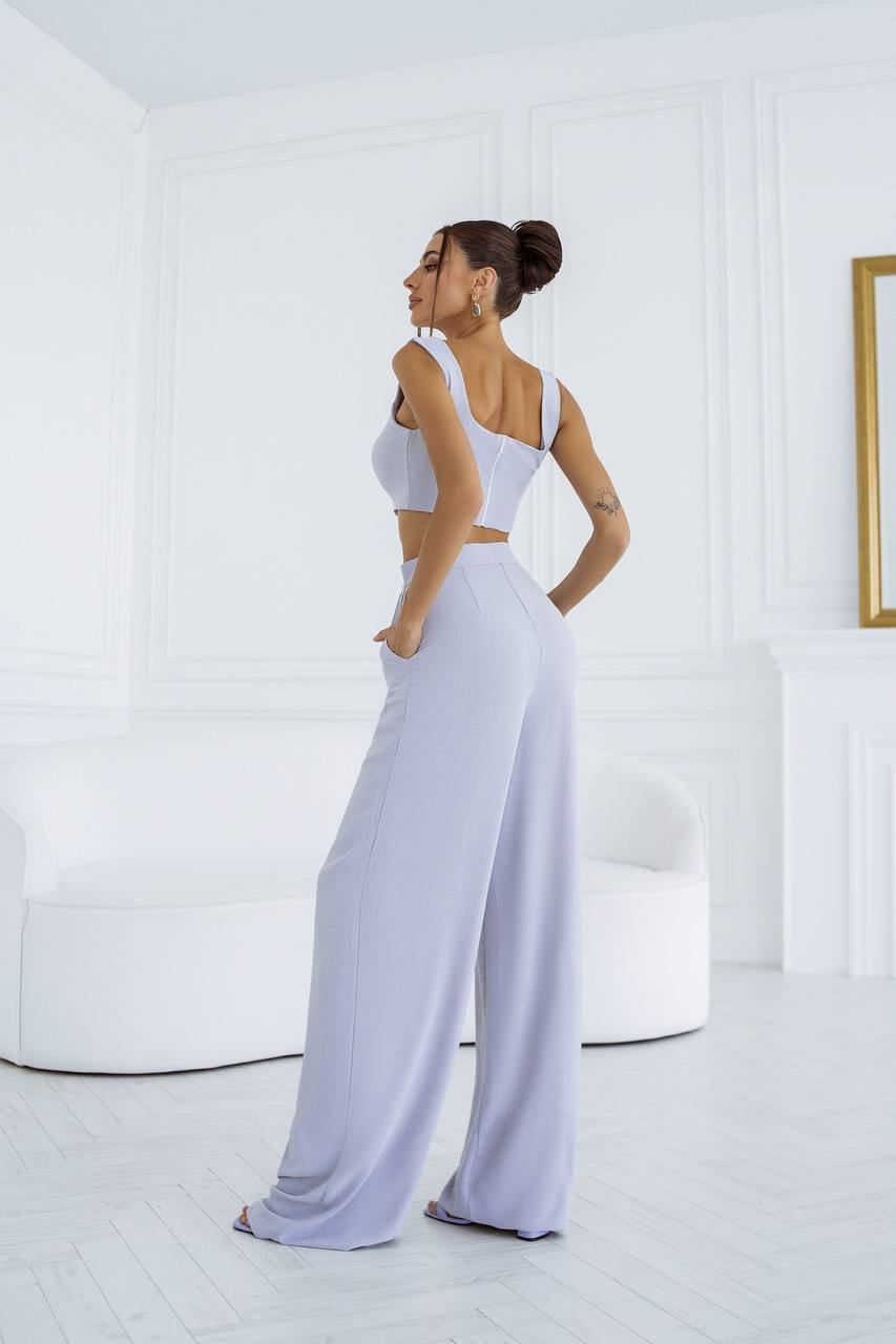Woman in a white outfit standing in a minimalistic room with a white wall and a gold-framed picture.