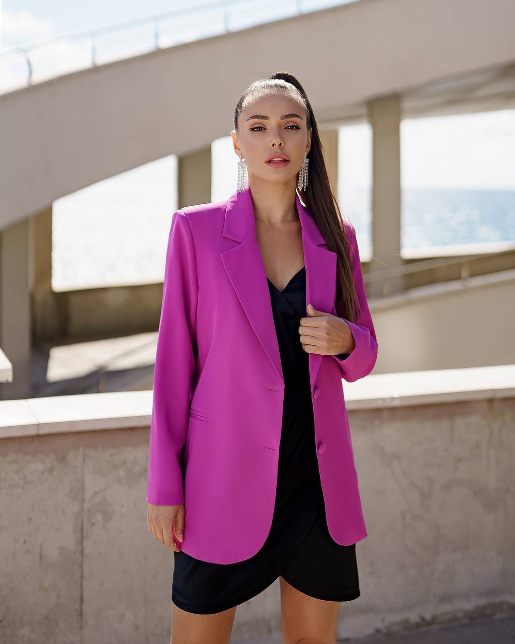 Woman wearing a bright pink blazer over a black dress outdoors.