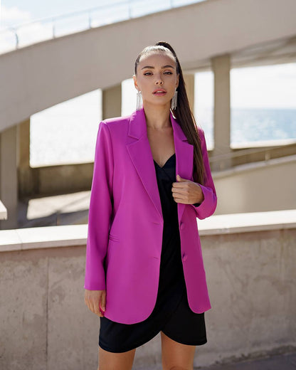 Woman wearing a bright pink blazer over a black dress outdoors.