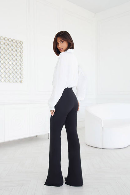 Woman wearing a white blouse and black pants in a minimalistic room.