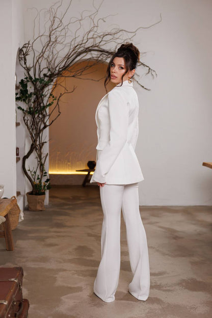 Woman in a white suit standing in an indoor setting with minimal decor.