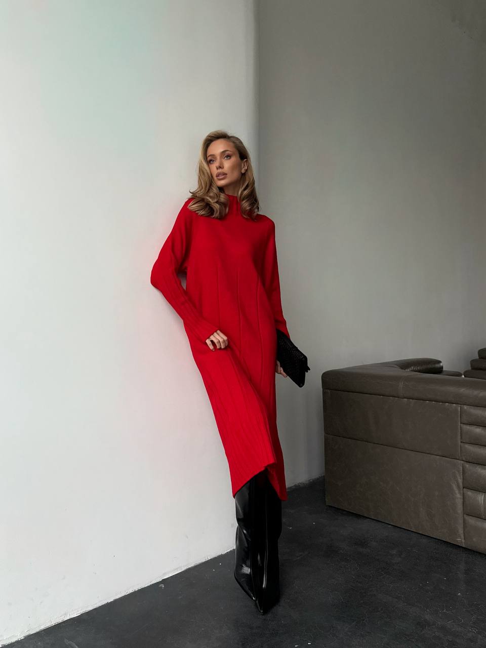 Woman in a red dress and black boots standing against a plain wall.