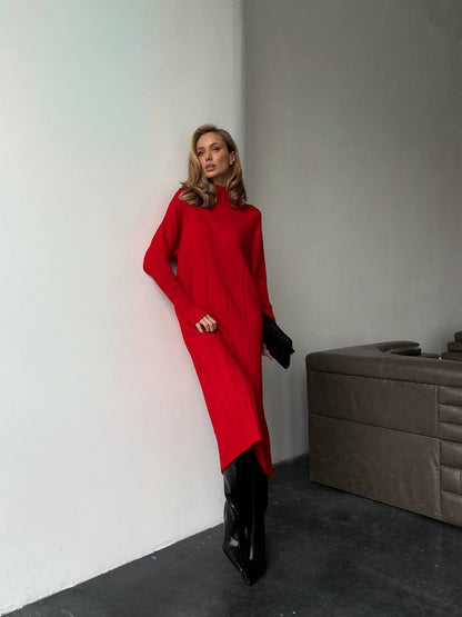 Woman in a red dress and black boots standing against a plain wall.