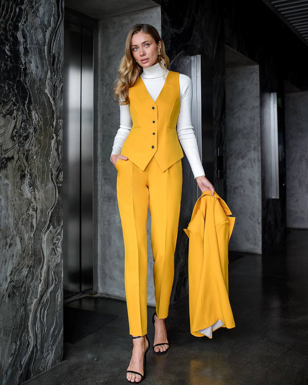 Woman in a yellow suit holding a matching jacket in a modern interior setting