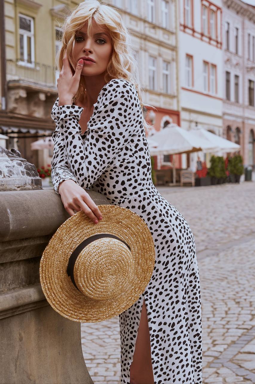 Woman in a polka dot dress holding a straw hat on a city street.