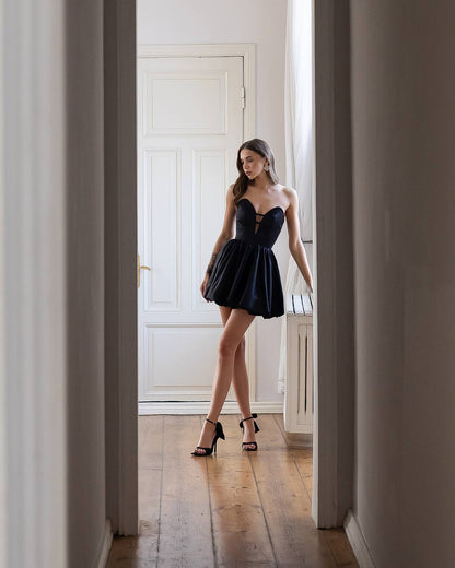 Woman in a black dress standing in a doorway of a well-lit room.