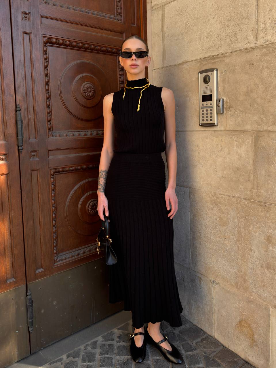 Woman in a black dress standing against a stone wall with a wooden door.