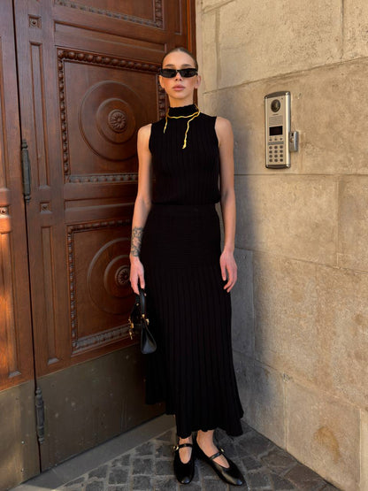 Woman in a black dress standing against a stone wall with a wooden door.