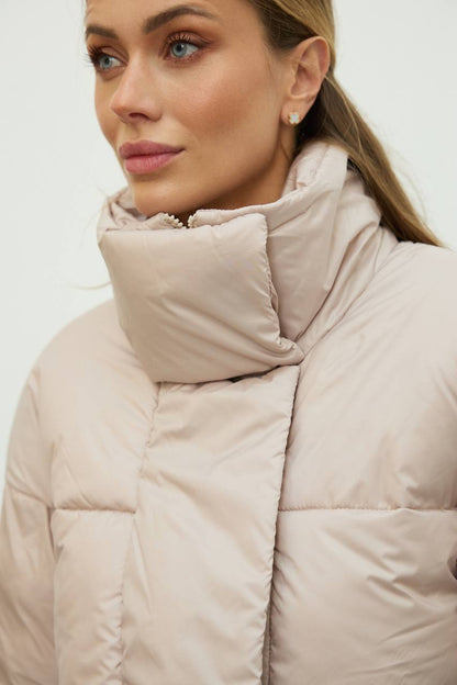 Woman wearing a beige puffer jacket against a white background