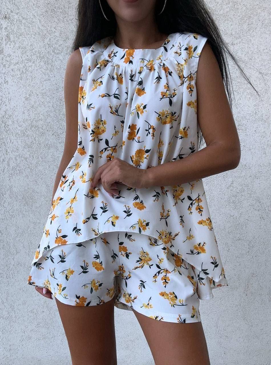 Woman wearing a white sleeveless top and shorts with yellow floral pattern against a plain background