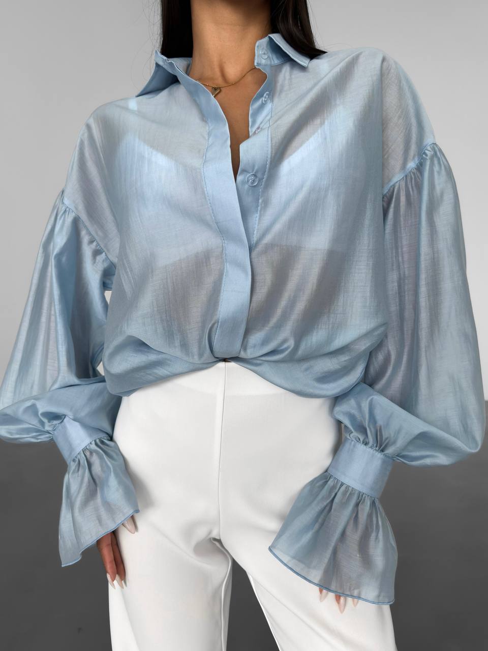Light blue blouse with puffed sleeves worn by a person on a gray background