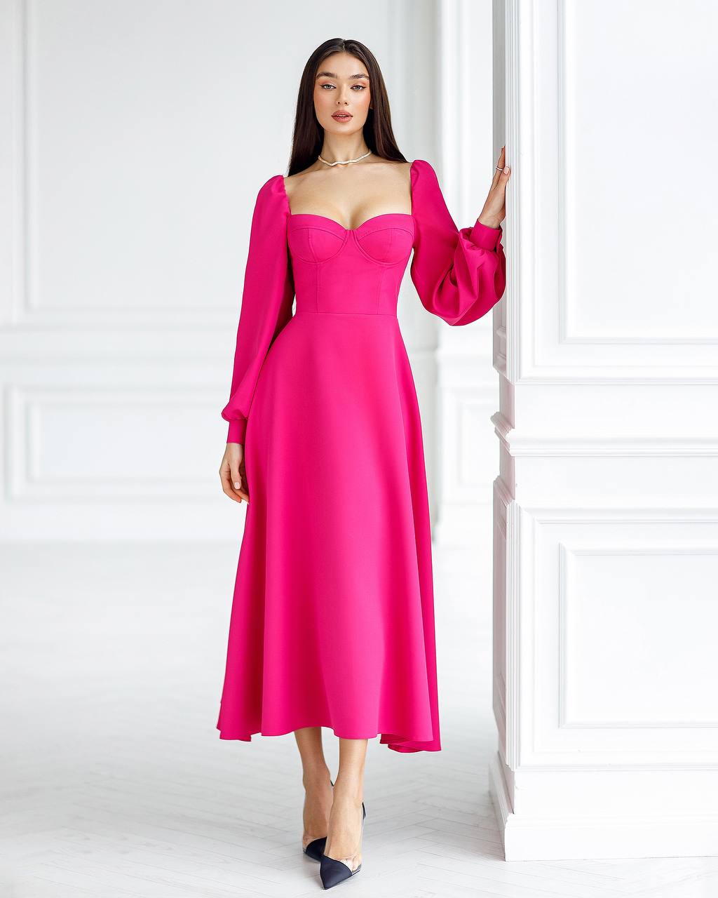Woman wearing a bright pink dress with long sleeves against a white wall.