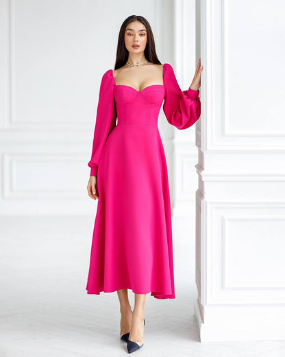 Woman wearing a bright pink dress with long sleeves against a white wall.