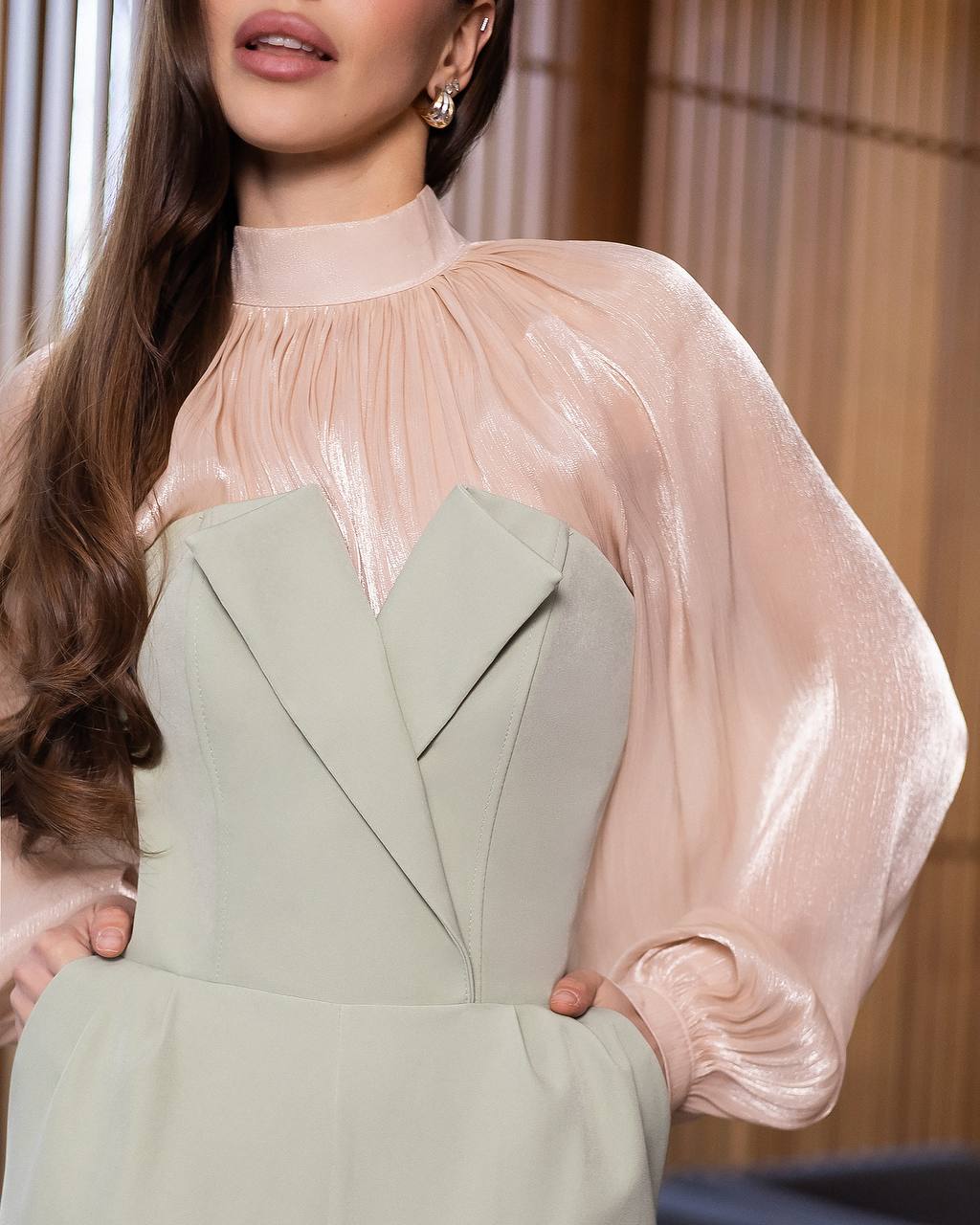 Woman wearing a light green dress with sheer pink sleeves against a neutral background