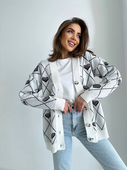 Woman wearing a patterned cardigan over a white shirt and light blue jeans on a plain background