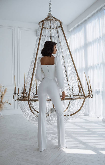 Woman in a white jumpsuit standing in a bright room with a decorative hanging chair.
