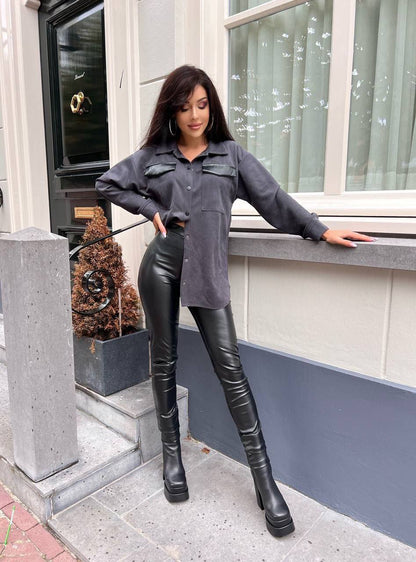 Woman in gray shirt and black leather pants standing on a sidewalk.