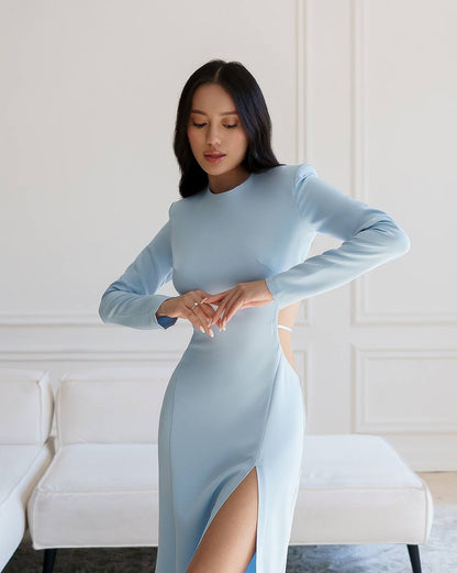 Woman wearing a light blue dress with a high slit in a room with white walls and furniture.