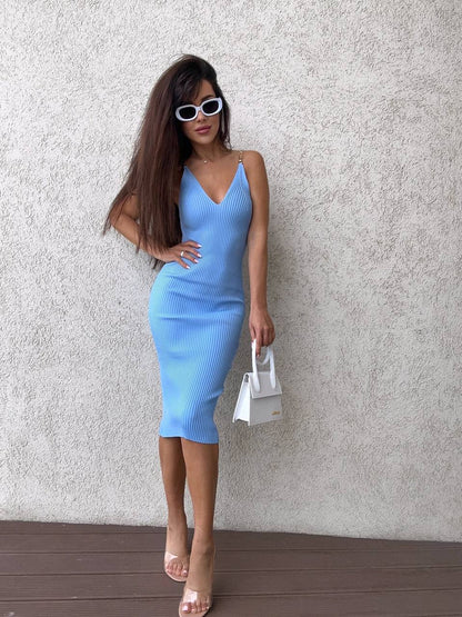 Woman in a blue dress holding a white handbag against a textured wall.